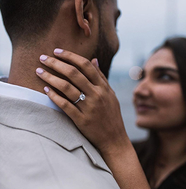 A couple shares an intimate moment, with one person gently holding the other's face, showcasing an engagement ring.