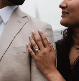 A close-up of a woman's hand resting on a man's suit jacket, showcasing an engagement ring.